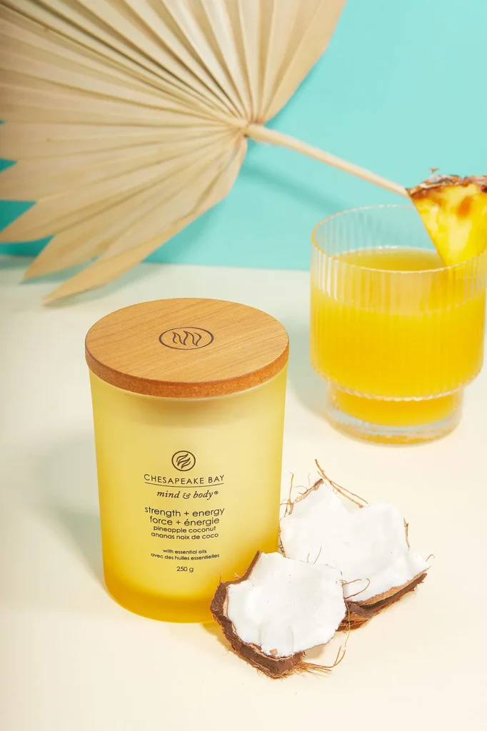 Home scent candle styled to showcase the aroma- beside fresh coconut, pineapple juice and a dried palm leaf – lifestyle product photography.