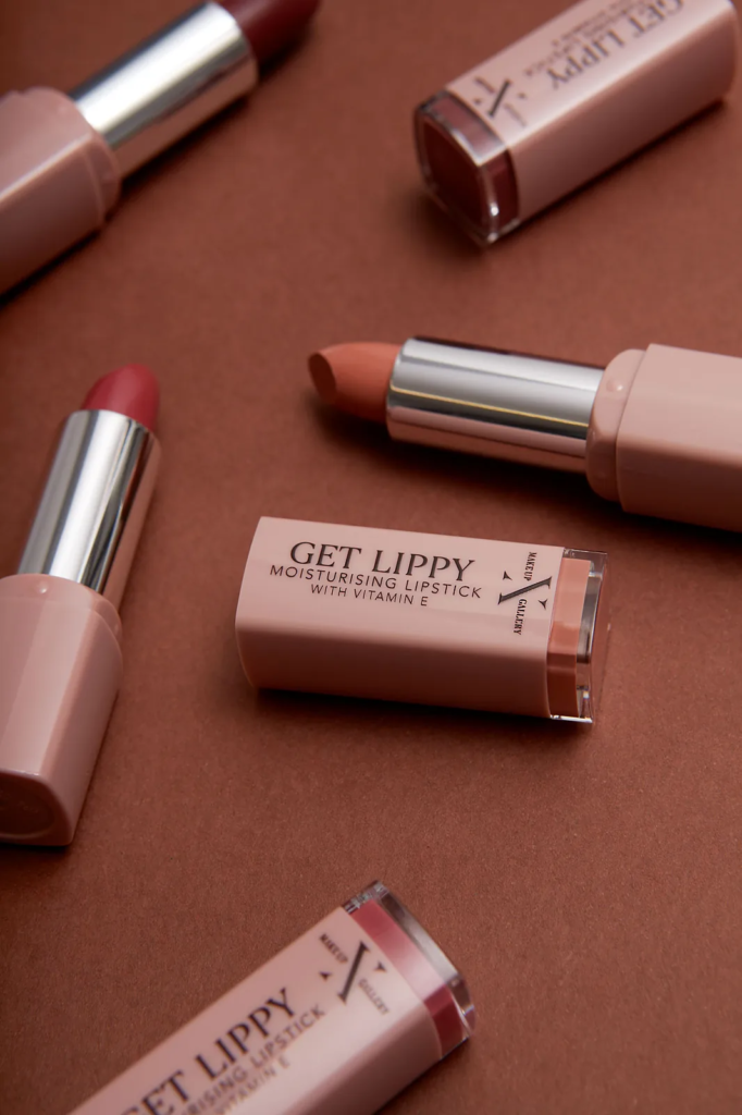 Styled product photography UK – nude and berry lipsticks in blush pink cases scattered across a terracotta backdrop in brand colours