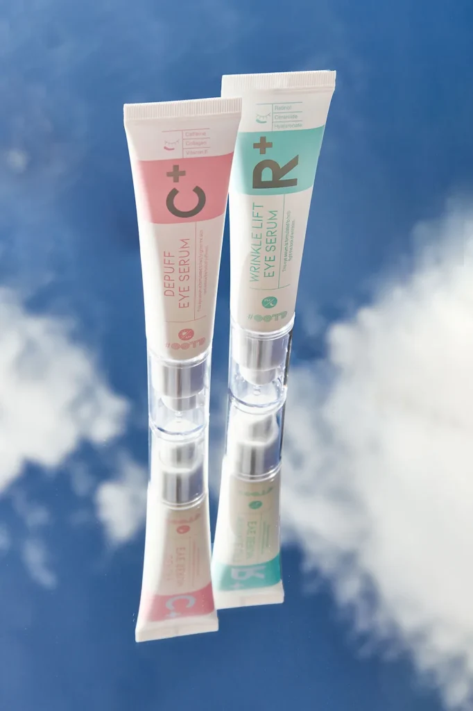 Creative styled product photography of two eye serum tubes standing on a mirror reflecting blue sky and clouds.